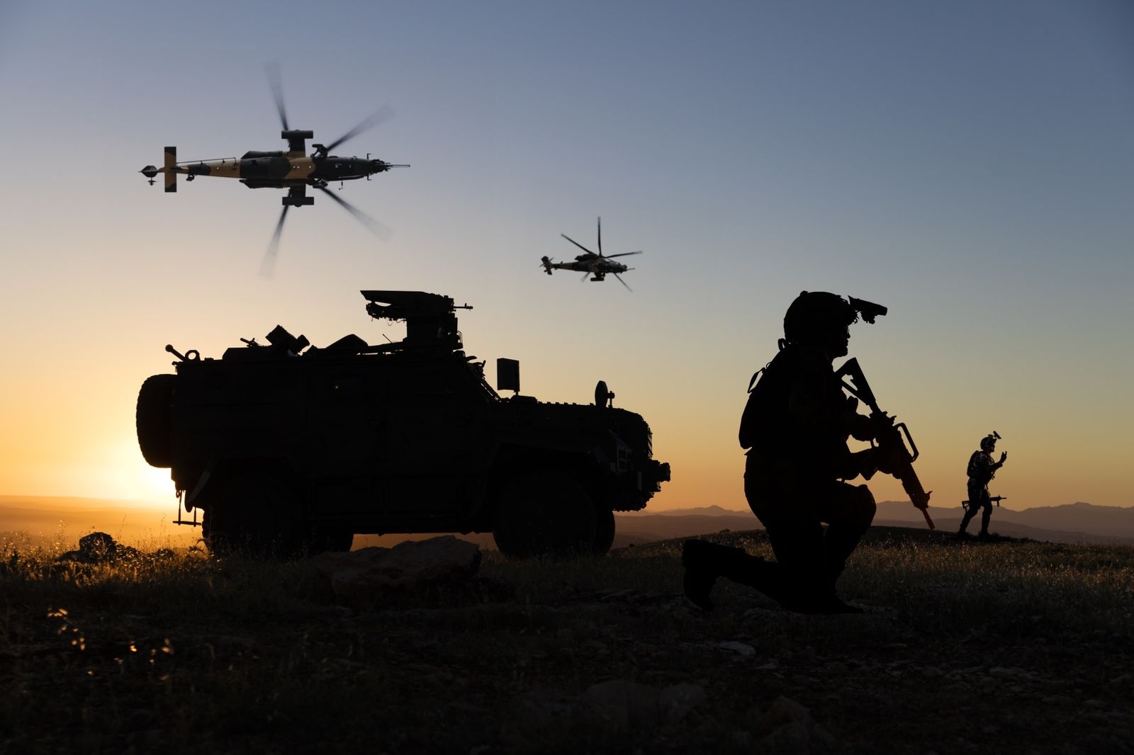 Defence forces silhouetted at sunset with armoured vehicle and military helicopters
